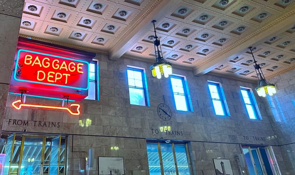 the interior of portland, oregon's train station. a blue and orange neon sign points the way to the baggage department.