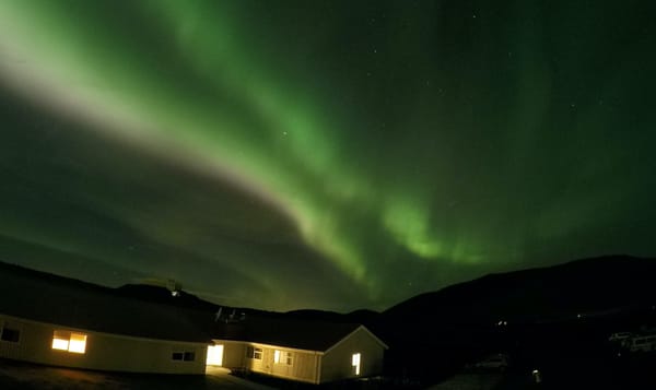 the northern lights shimmer in green, yellow, and pink over a small house in iceland.