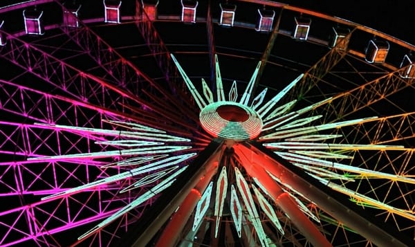 spokes of a ferris wheel lit up in purple, green, and orange