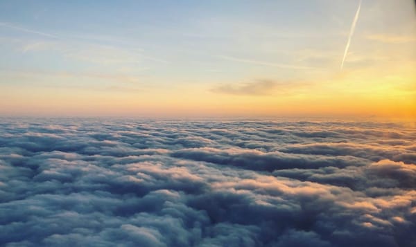 a photo of the view from a plane above a layer of bumpy cloud cover. a sunrise peeks over the scene from the right. streaks o