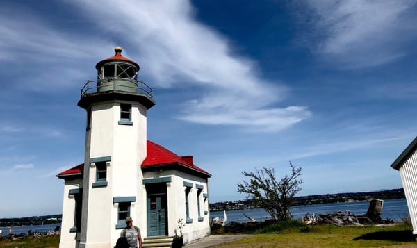 a photo of a white lighthouse with a red roof sits against a deep blue sky with streaks of clouds.