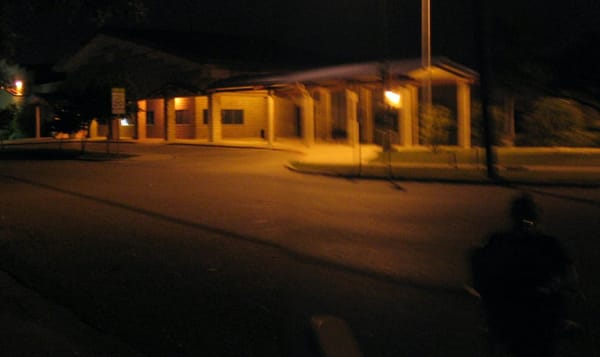 a blurry photo of an elementary school building at night, in a small town in central Texas. the darkness is illuminated with 