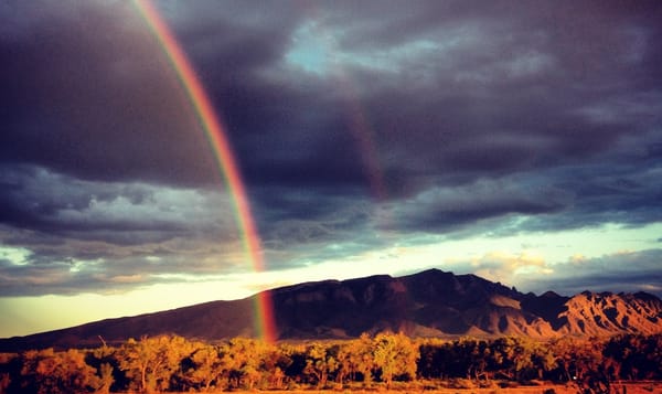 a photo of the mountains outside Albuquerque, New Mexico. above the mountains in the shadows of dusk sit dark clouds with fle