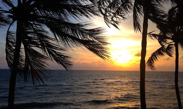 the sun surrounded by evening clouds sets over the Indian ocean. waves lap gently against a beach that's near out of frame. t