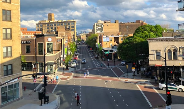 a city street viewed from a few stories up, with buildings, cars, and people