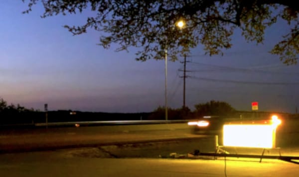 a marquee sign on the side of the road with a car driving behind it.