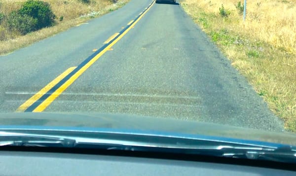 a two-lane road viewed through a car windshield