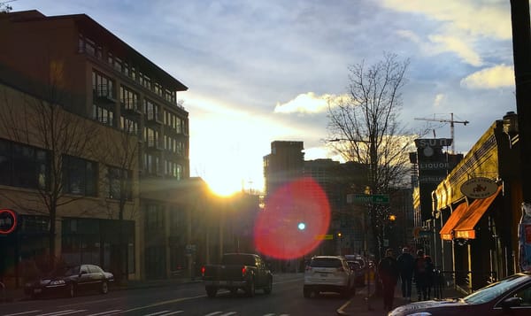 a neighborhood street with cars, shops, and people