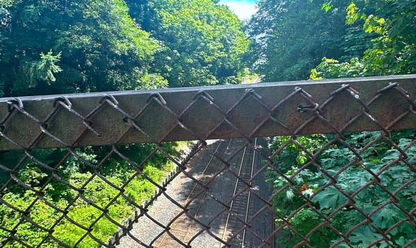 view of train tracks from a bridge through a chain link fence