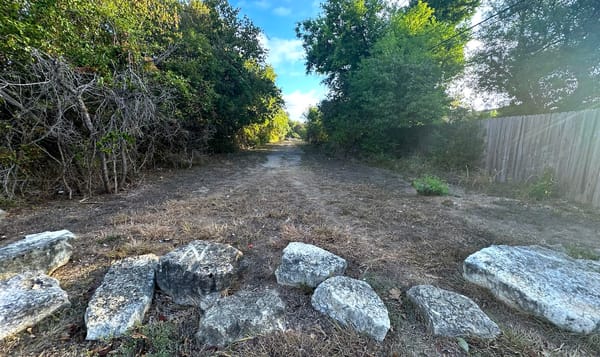 a path into the woods with large rocks strewn across the entrance