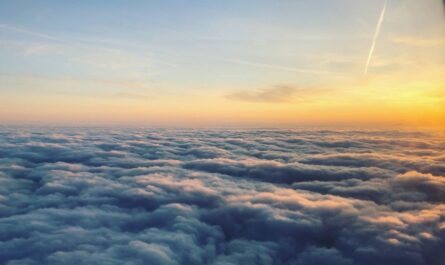 a photo of the view from a plane above a layer of bumpy cloud cover. a sunrise peeks over the scene from the right. streaks of clouds texture the sky.