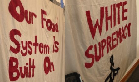 a photo of a large white sheet turned into a hand-painted banner. in red paint, the lettering reads, "Our Food System Is Built On WHITE SUPREMACY." they're not wrong!!