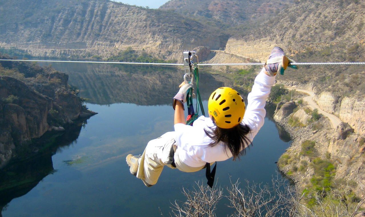 a woman riding a zipline across a canyon