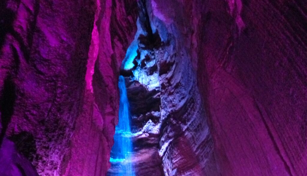 a photo of ruby falls, a high waterfall inside a cavern that are lit up magenta and blue