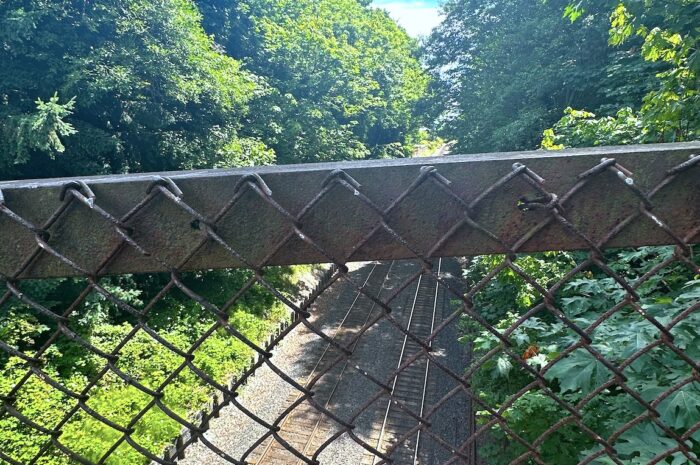 view of train tracks from a bridge through a chain link fence