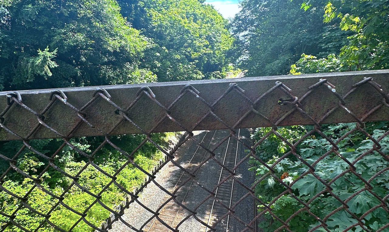 view of train tracks from a bridge through a chain link fence