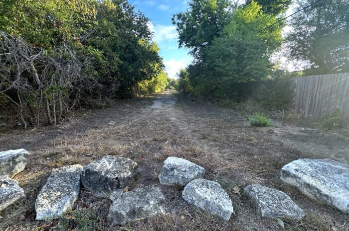 a path into the woods with large rocks strewn across the entrance