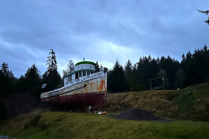 a rusting boat sits on land - a small hill next to a taller hill